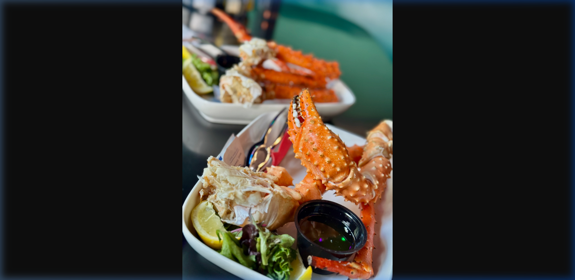 Fresh Alaska king crab claws and legs on a white plate with drawn butter dipping sauce, lemon wedge, and greens — served at Humpy's Great Alaskan Alehouse in downtown Anchorage